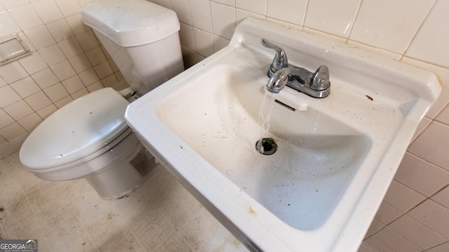 half bath with toilet, tile walls, and a sink