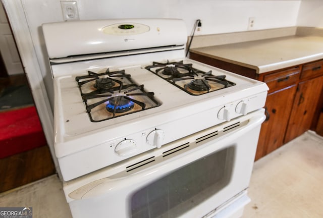 interior details with brown cabinets, white gas range oven, and light countertops