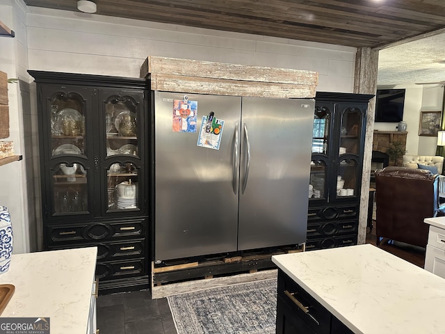 kitchen featuring freestanding refrigerator, a stone fireplace, light stone counters, and dark cabinetry