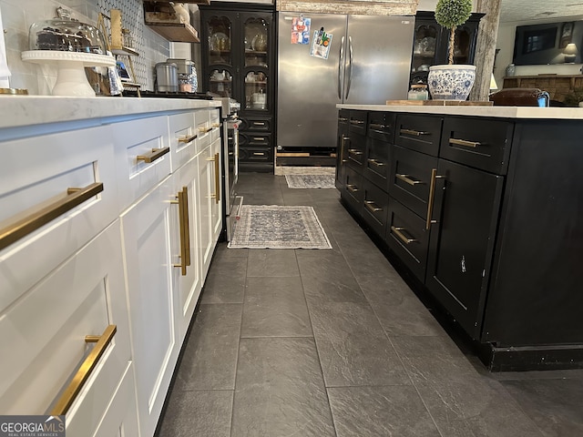 kitchen with dark cabinetry, light countertops, freestanding refrigerator, white cabinetry, and dark tile patterned floors