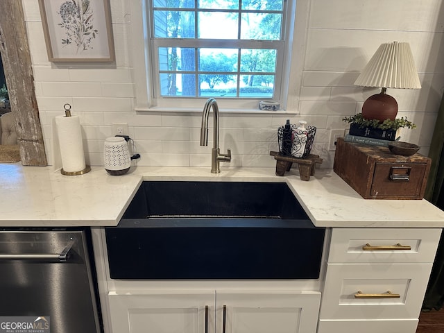 kitchen featuring stainless steel dishwasher, a sink, white cabinets, and tasteful backsplash