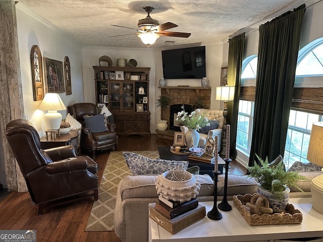 living area with ceiling fan, a textured ceiling, crown molding, a fireplace, and wood finished floors