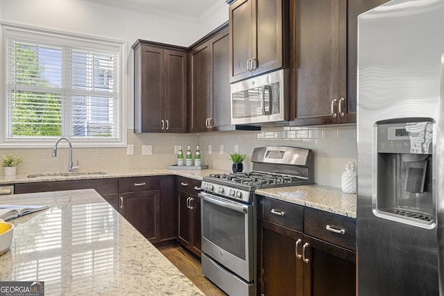 kitchen with crown molding, dark brown cabinets, a sink, appliances with stainless steel finishes, and a wealth of natural light