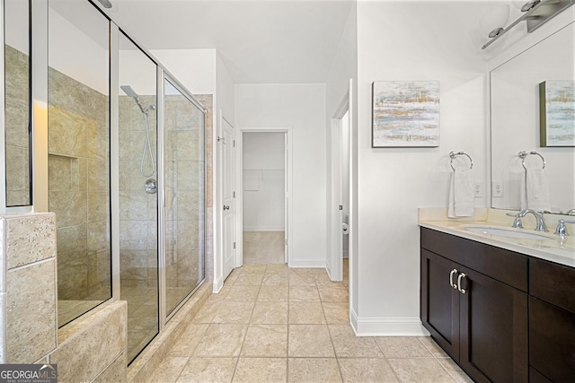 bathroom featuring vanity, baseboards, a walk in closet, tile patterned floors, and a shower stall
