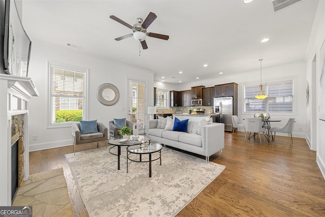 living area featuring crown molding, a fireplace, a ceiling fan, baseboards, and visible vents