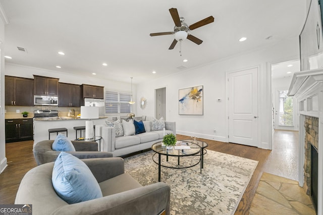 living area with ceiling fan, visible vents, ornamental molding, and a fireplace