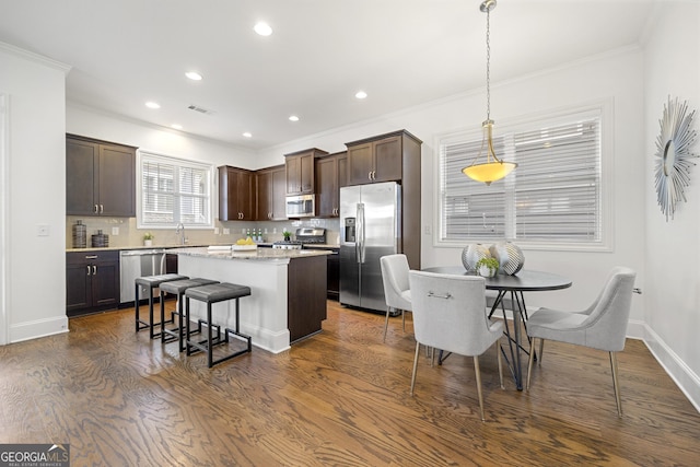 kitchen with dark brown cabinetry, a kitchen island, a kitchen bar, backsplash, and appliances with stainless steel finishes