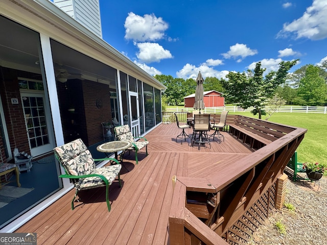 wooden terrace featuring a lawn, fence, outdoor dining space, and a sunroom
