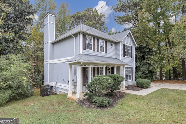 traditional home featuring a chimney, a front yard, covered porch, and a shingled roof