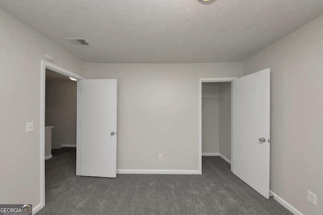 unfurnished bedroom with a textured ceiling, baseboards, visible vents, and dark carpet