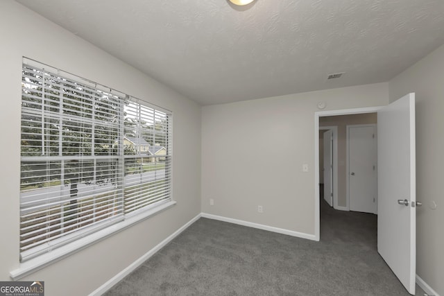 carpeted spare room with a textured ceiling, baseboards, and visible vents