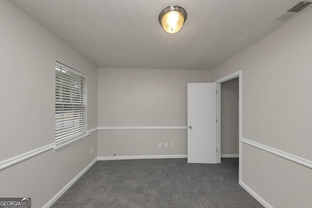 empty room featuring carpet flooring, a textured ceiling, visible vents, and baseboards