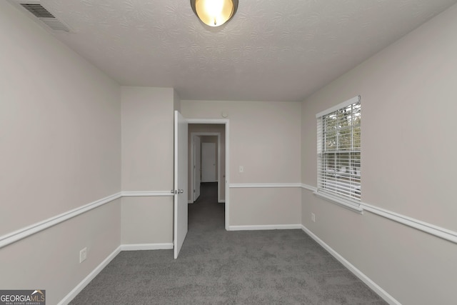 empty room featuring a textured ceiling, carpet floors, baseboards, and visible vents