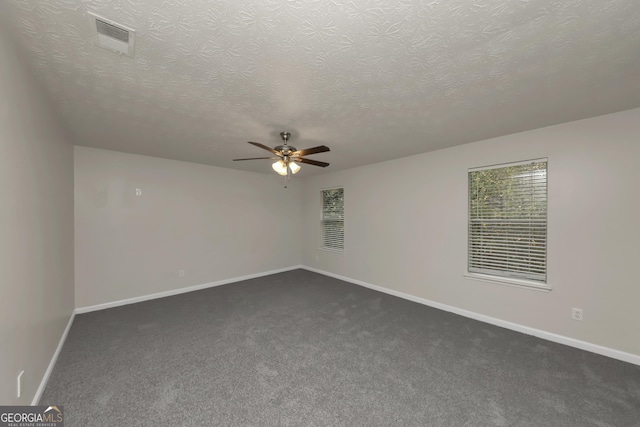 spare room featuring a ceiling fan, dark carpet, visible vents, and a textured ceiling