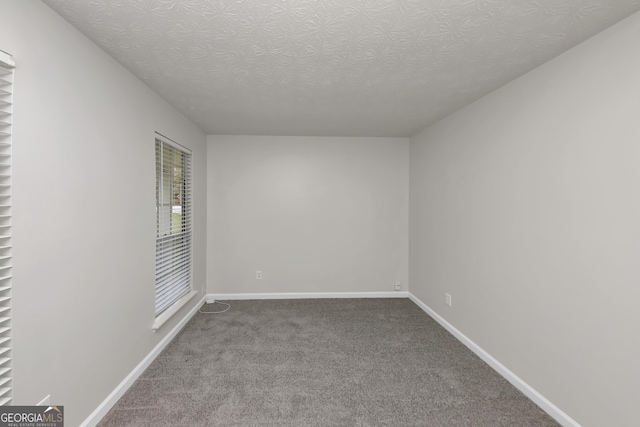 empty room with carpet, baseboards, and a textured ceiling