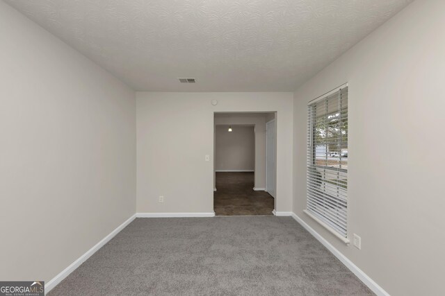 empty room with a textured ceiling, carpet, baseboards, and visible vents