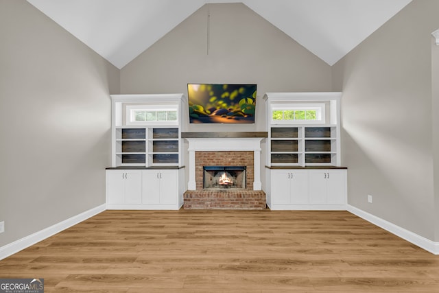 unfurnished living room with baseboards, a brick fireplace, wood finished floors, and high vaulted ceiling
