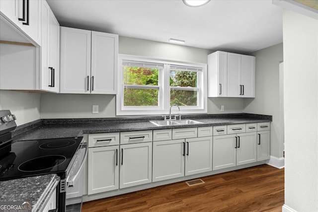 kitchen with electric range, dark countertops, a sink, dark wood-type flooring, and visible vents