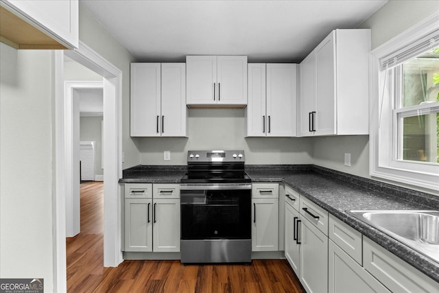 kitchen featuring stainless steel electric range oven, dark countertops, dark wood finished floors, and white cabinets