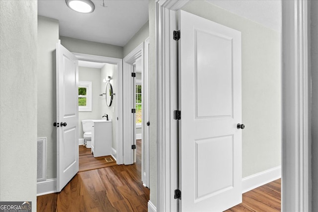 corridor with baseboards, wood finished floors, and visible vents