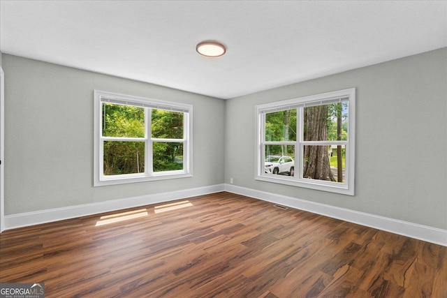 unfurnished room with a healthy amount of sunlight, baseboards, wood finished floors, and visible vents