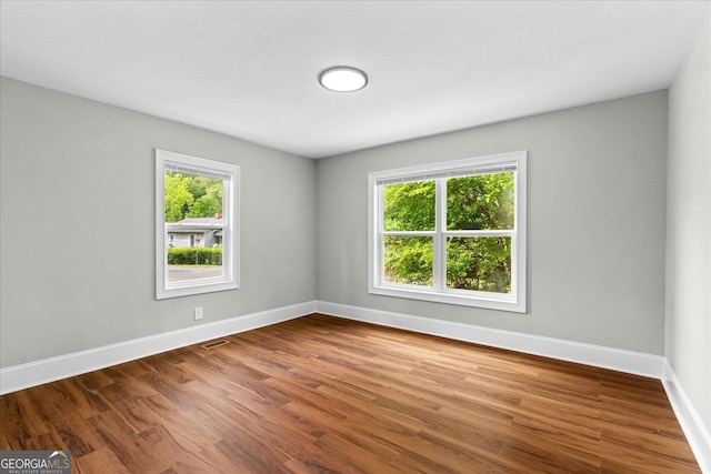 spare room featuring baseboards, visible vents, plenty of natural light, and wood finished floors