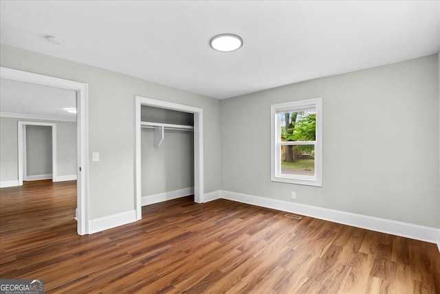 unfurnished bedroom featuring baseboards, visible vents, wood finished floors, and a closet