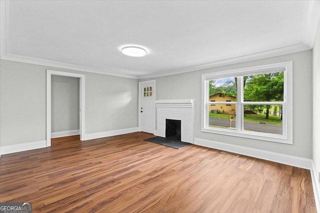 unfurnished living room featuring visible vents, crown molding, a brick fireplace, wood finished floors, and baseboards