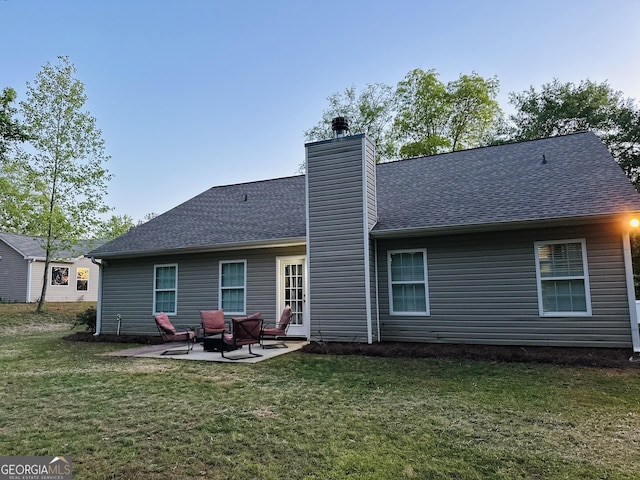 back of house with a patio area, a lawn, a chimney, and roof with shingles