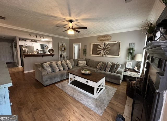living room with a ceiling fan, a textured ceiling, ornamental molding, and dark wood finished floors