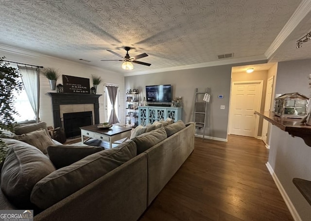 living room featuring a ceiling fan, baseboards, a tile fireplace, dark wood-type flooring, and ornamental molding