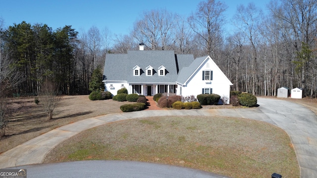 new england style home featuring curved driveway, a chimney, and a porch