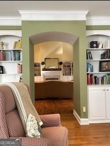 living area with crown molding, built in shelves, arched walkways, and wood finished floors