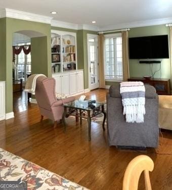 living area featuring crown molding, arched walkways, built in features, and wood finished floors