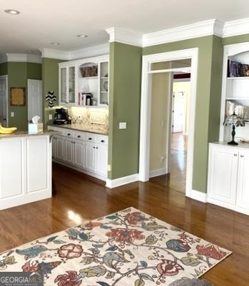 kitchen with light countertops, ornamental molding, dark wood finished floors, and glass insert cabinets