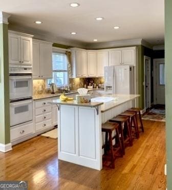 kitchen with white appliances, white cabinets, a center island, and light wood-type flooring