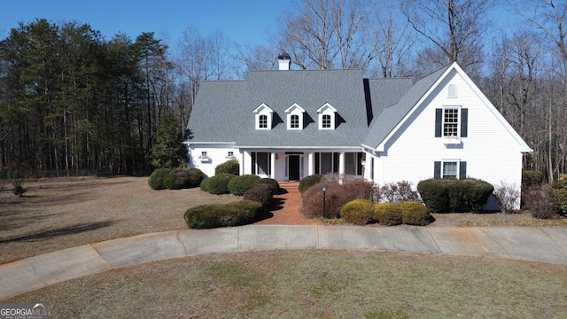 cape cod house with a shingled roof, a front lawn, covered porch, and a chimney