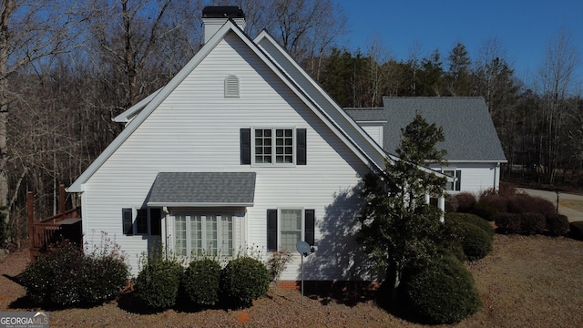 view of front of home with a forest view, a chimney, and roof with shingles
