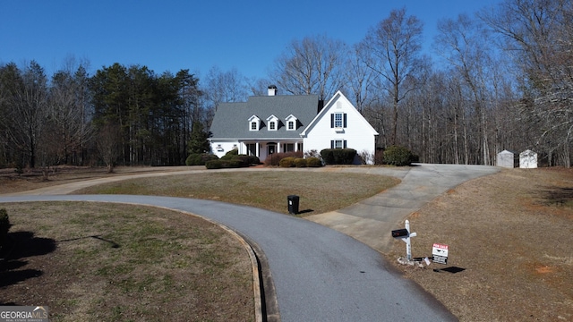 view of front of property with curved driveway, a chimney, and a front yard