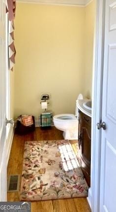 half bath with visible vents, wood finished floors, toilet, and vanity