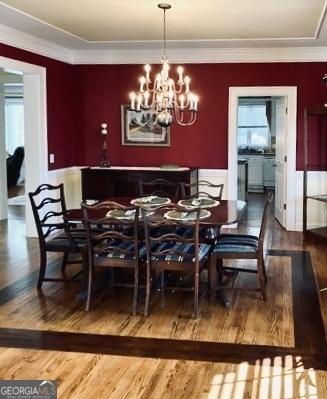 dining space with plenty of natural light, ornamental molding, wood finished floors, and a chandelier