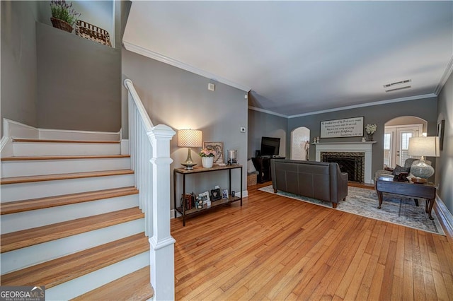 staircase featuring arched walkways, hardwood / wood-style flooring, crown molding, a fireplace, and baseboards