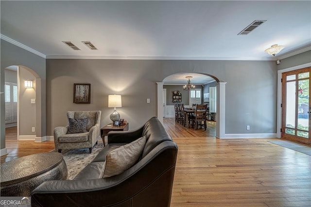 living room with arched walkways, light wood-style flooring, crown molding, a chandelier, and baseboards
