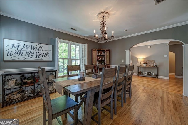 dining room featuring arched walkways, light wood-style floors, a chandelier, baseboards, and crown molding