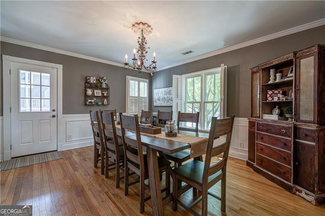 dining room with a chandelier, light wood finished floors, wainscoting, a decorative wall, and crown molding
