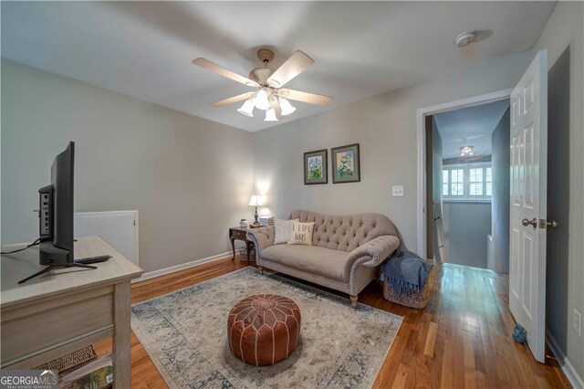 living room with wood finished floors, a ceiling fan, and baseboards