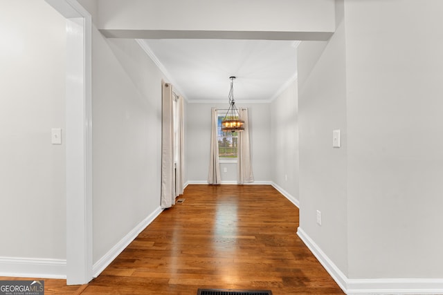unfurnished dining area featuring baseboards, ornamental molding, wood finished floors, and a notable chandelier