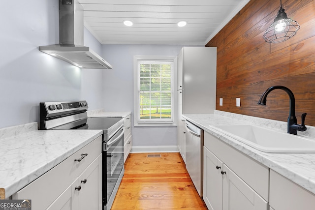 kitchen with baseboards, wall chimney range hood, white cabinets, a sink, and stainless steel appliances