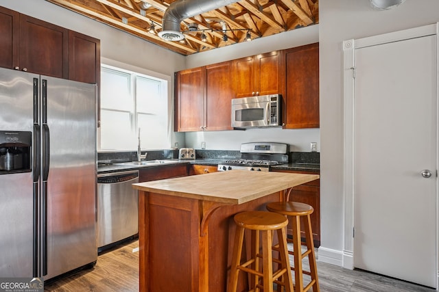 kitchen with stainless steel appliances, butcher block counters, a sink, wood finished floors, and a breakfast bar area