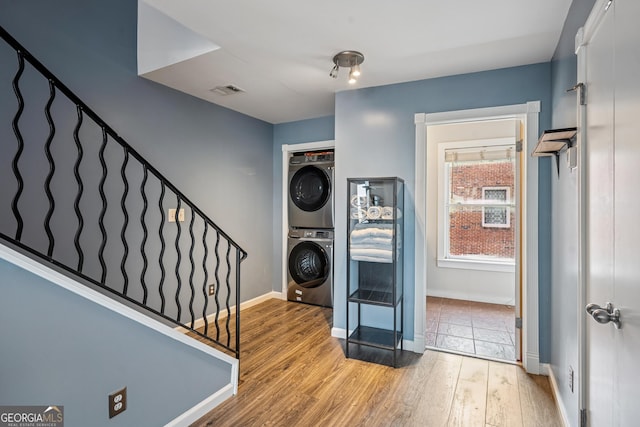 laundry area featuring stacked washing machine and dryer, light wood-style floors, and baseboards